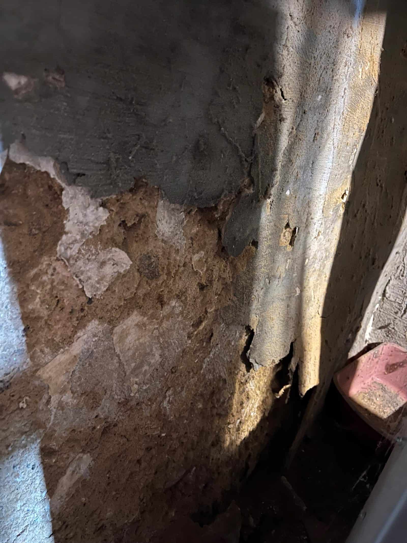 Deteriorated painted plaster and substrate on a basement wall, with paint separating from the surface