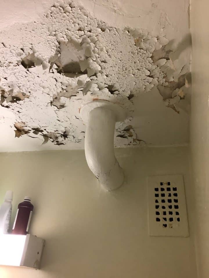 Severely deteriorated and peeling paint on a bathroom ceiling around a plumbing stack