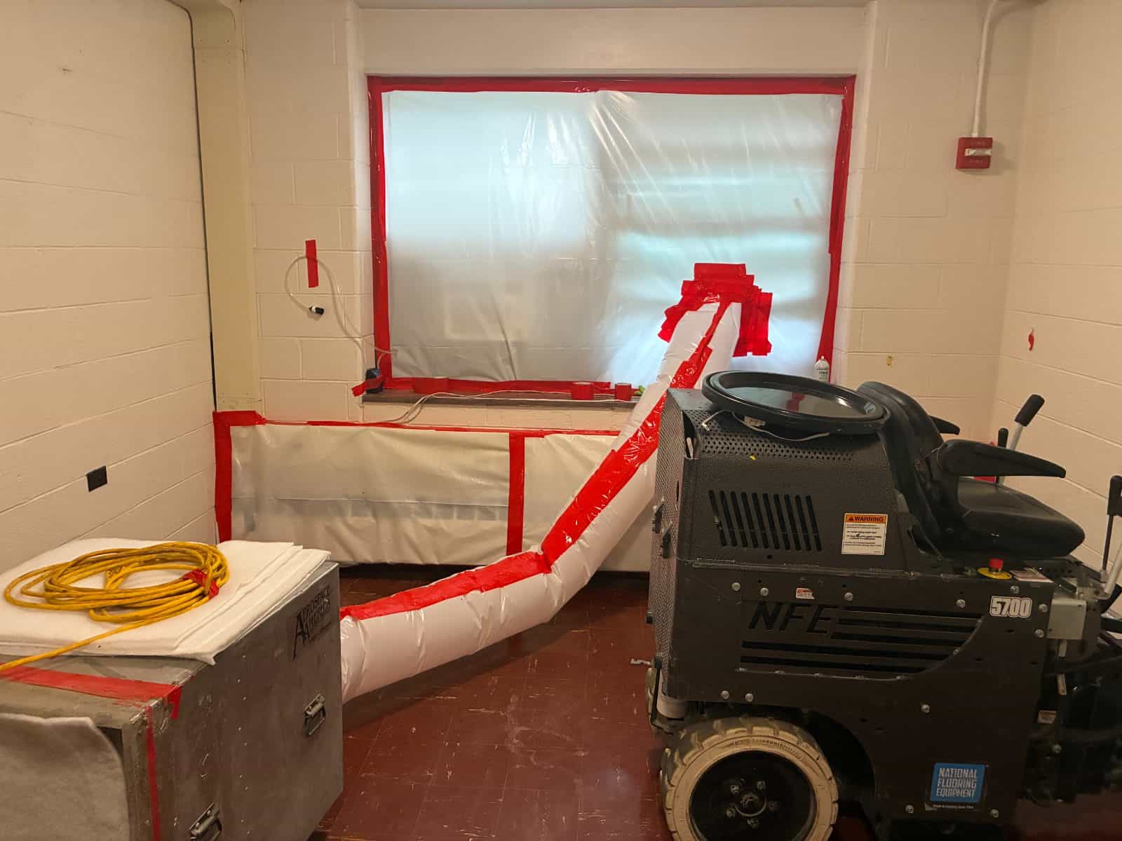 Negative air machine ducted through a sealed window opening, with polyethylene sheeting and taped seams isolating the work area