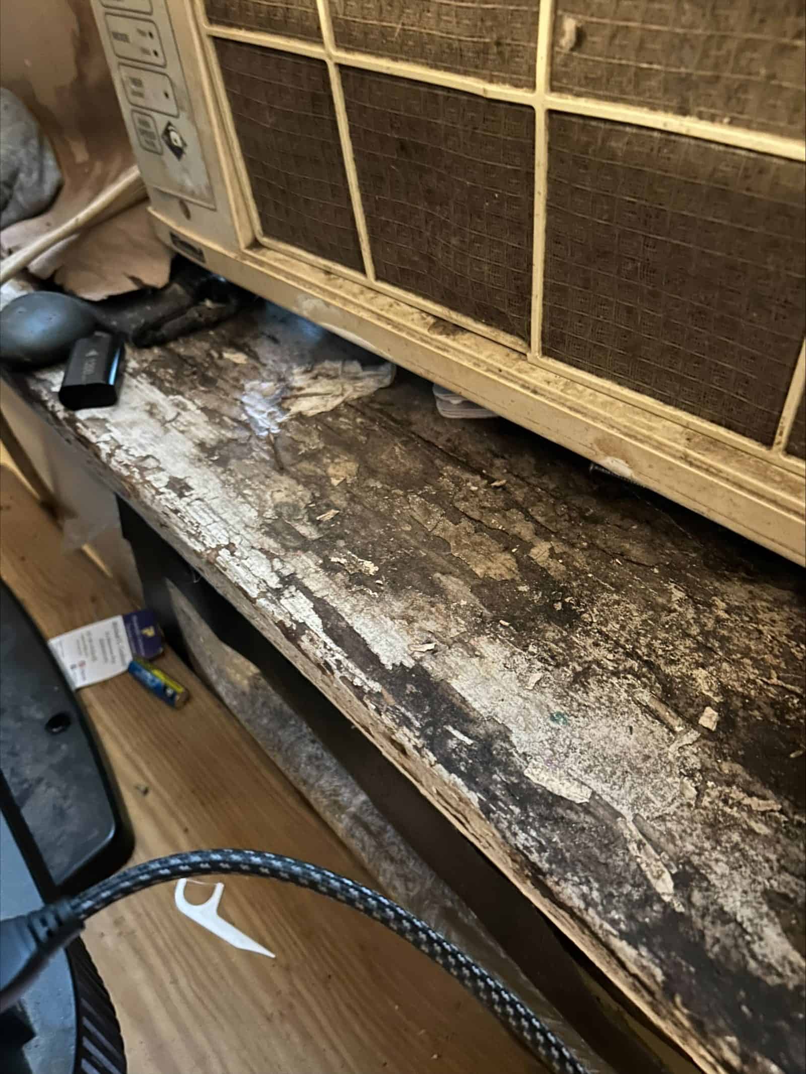 Deteriorated window sill beneath a through-wall air conditioning unit, with saturated and delaminating material